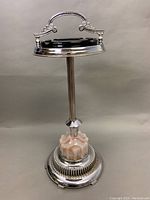Full view of the floor ashtray showing the metal stand with ornate handle, smoked glass ashtray removable insert, and pink and white scalloped glass base.