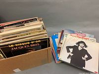 Box filled with a variety of vinyl record albums including French Jacques Brel and others.