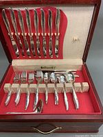 Top view of wooden chest showcasing flatware including knives, forks, spoons neatly secured with straps inside red cloth lining.