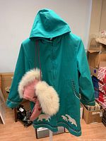 Greenish-blue long spring jacket with hood, decorated with white polar bear patterns near hem and black and white trim on cuffs and pockets, shown with pink mitts with white fur trim.