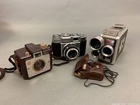 Group shot showing four vintage cameras and accessories, including Kodak Brownie, Kodak Holiday flash, Zeiss Ikon Contina camera, and 8mm turret camera.