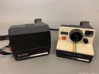 Pair of Polaroid cameras: black Sun 660 Autofocus and cream OneStep Land Camera side by side