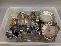 Top-down view of all silver plate items in a plastic bin showing trays, candlesticks, goblets, salt and pepper shakers, and a napkin ring.