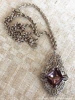 Full view of the antique pendant with the purple glass stone and connected rolo link chain laid out on fabric background.
