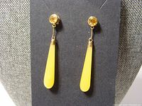 Pair of 14K yellow gold earrings with elongated yellow jade tear drop dangles and round citrine stones at the studs shown on a jewelry stand.