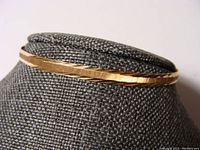 Oblique view of 18K gold bangle on display form showing faceted pattern