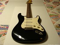 Full view of black Squire style electric guitar showing body, neck, and headstock with white pickguard and control knobs