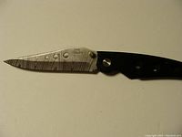 Closed and partially opened view of Damascus steel folding knife blade with black handle and belt clip.