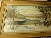 Full view of the landscape oil painting on board showing a winter scene with frozen water, trees, and mountains in the background.