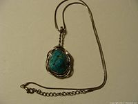 Full view of turquoise pendant on silver chain laid flat showing twisted silver border setting and snake chain with clasp.