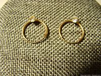 Pair of small yellow gold hoop earrings each with a clear rhinestone, shown lying flat on fabric background.