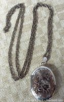 Sterling silver chain and oval photo locket showing detailed floral engraving on front and chain length.