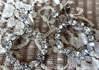 Photo showing the front side of both silver-tone earrings with clear round and marquise Swarovski crystals forming circular hoops on a lace background.