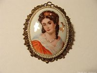 Front view of the oval Limoges porcelain brooch featuring a hand-painted portrait of a woman with pearls and filigree metal frame.