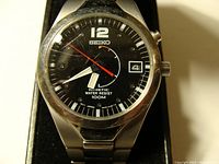 Front view of Seiko Kinetic watch showing black dial, date window, and scratched crystal.