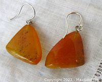 Close-up of earrings showing amber stones and sterling silver ear wires on light textile background.