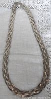 Full view of the flat braided sterling silver necklace laid out on fabric surface: shows entire length, width, and braided pattern.