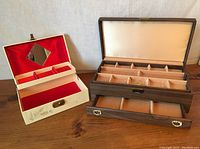 Photo showing open beige jewellery box with red interior, mirror, and compartments alongside open large brown wood grain jewellery box with gold interior compartments and pull-out drawer.