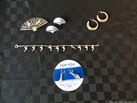 All items shown on a dark gingham fabric background, including fan-shaped brooch, fan earrings, small hoop earrings, dolphin charm bracelet, and dangle pendant earrings on original card.
