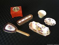 Full view of the porcelain vanity set including all six items arranged on a black textured surface showing the brushes, trinket container, cup, dish, and tray.