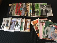 Lot of vintage sewing pattern envelopes arranged on a black surface, including men's and women's patterns from the 1950s and 1960s.