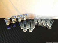 All 17 items displayed: 4 pedestal mugs with blue bases and scenic lighthouse design and grouped mid-century crystal glasses including cooler and sling types.