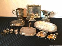Full lot overview showing water pitcher, square silver tray, silver crumb pan with wood handle, small serving trays, silver napkin rings, and holders.
