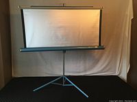 Full view of the projector screen mounted on its tripod stand showing screen surface and legs.