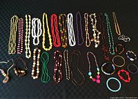 Full overview of costume jewelry including strands of beads in multiple styles and colors laid flat on a dark background.