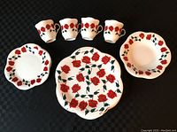 Four mugs, two small plates, and one large plate with red rose pattern and Betty Boop trademark, all displayed on black surface.
