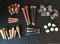 Wooden legs of various sizes and styles along with metal caster wheels spread on black fabric