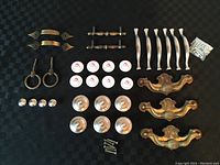 Overview of all hardware knobs and pulls arranged on black background showing 6 modern curved pulls, 3 ornate metal pulls, 6 ceramic rose knobs, 4 ring pulls, 4 round metal knobs, 2 pairs short metal pulls, and small screws.