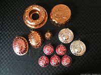 Top-down view showing all 12 copper molds in a group, highlighting the variety in size, design, and color tones (copper and silver).