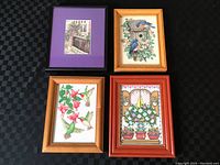 Four framed cross stitch artworks including birds and a garden scene seen from above on a black checkered surface