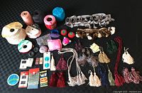 Lot overview showing a variety of sewing materials including ribbons, spools, tassels, pin cushions, needles, metal clips, and buttons arranged on a black surface.