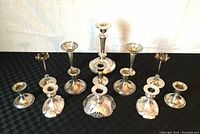 Front view of ten silver plated candle holders arranged together, showing different heights and designs