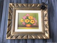 Oil painting with yellow-orange and pink flowers in vase framed with ornate wooden frame.