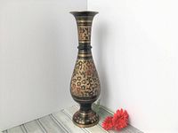 Full upright view of the tall etched brass vase with black and red pattern, showing overall shape and design