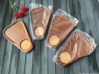 Four triangular wooden snack trays with cork coasters, three wrapped in plastic, one unpackaged, shown on dark wooden surface with red flowers.