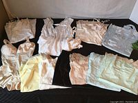Lot of women's satin and silk slips and bodysuit laid out on black surface showing various colors and styles.