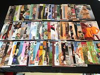 Wide layout of over 80 assorted knitting and crocheting pattern booklets and magazines arranged on a dark surface.