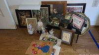 Overall view of the lot including framed ballet art, vintage figurines, and hand stitched textile art on wooden floor.