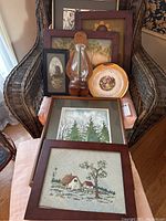Overall view of seven framed art pieces and one candle sconce on wicker chair and nearby surfaces