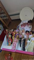 Multiple vintage Barbie dolls in a box along with a round white 1969 World of Barbie carrying case and some doll clothes.