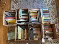 Seven boxes filled with books photographed from above on a rug.