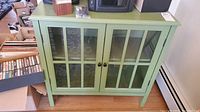 Front view of sage green display cabinet with double glass paneled doors showing interior shelving.