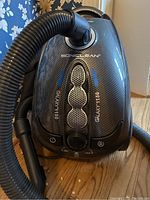 Top-down photo showing black Soniclean Galaxy 1150 canister vacuum cleaner, carbon fiber pattern, control knob, and hose attachment.