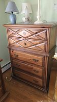 Front view of the vintage wooden chest of drawers highlighting carved drawer fronts, metal handles, and keyhole on top drawers.