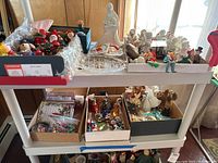 Various Christmas angels, figurines, ornaments, and decor displayed on white shelves and in open boxes.