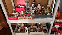 Multiple boxes on shelf containing a mix of vintage Christmas ornaments, figurines, and tinsel.